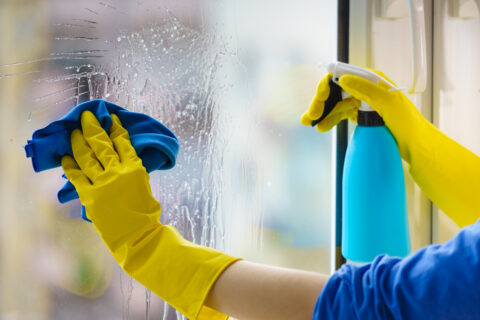 Gloved hand cleaning window rag and spray